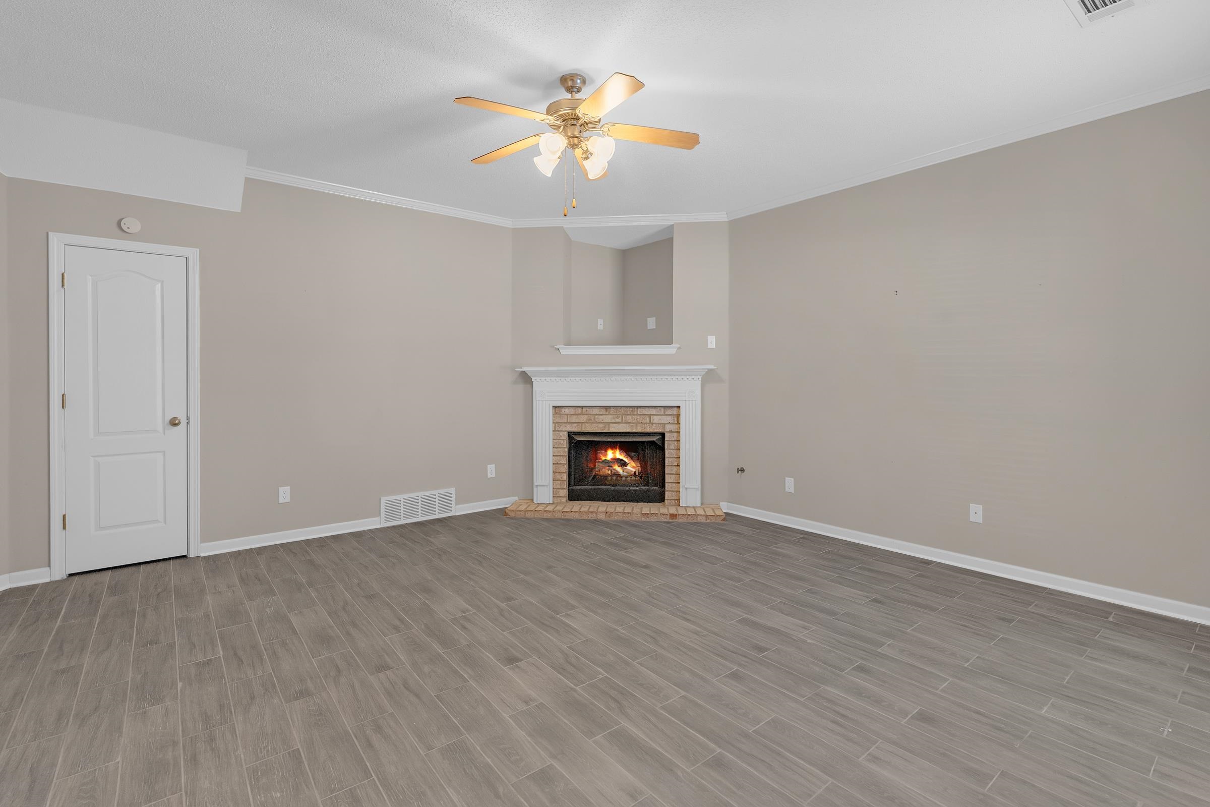 1229 North Sanga Road Memphis, TN 38016 - Photo 2 of 32 Unfurnished living room featuring crown molding, wood tiled floors, a brick fireplace, and ceiling fan