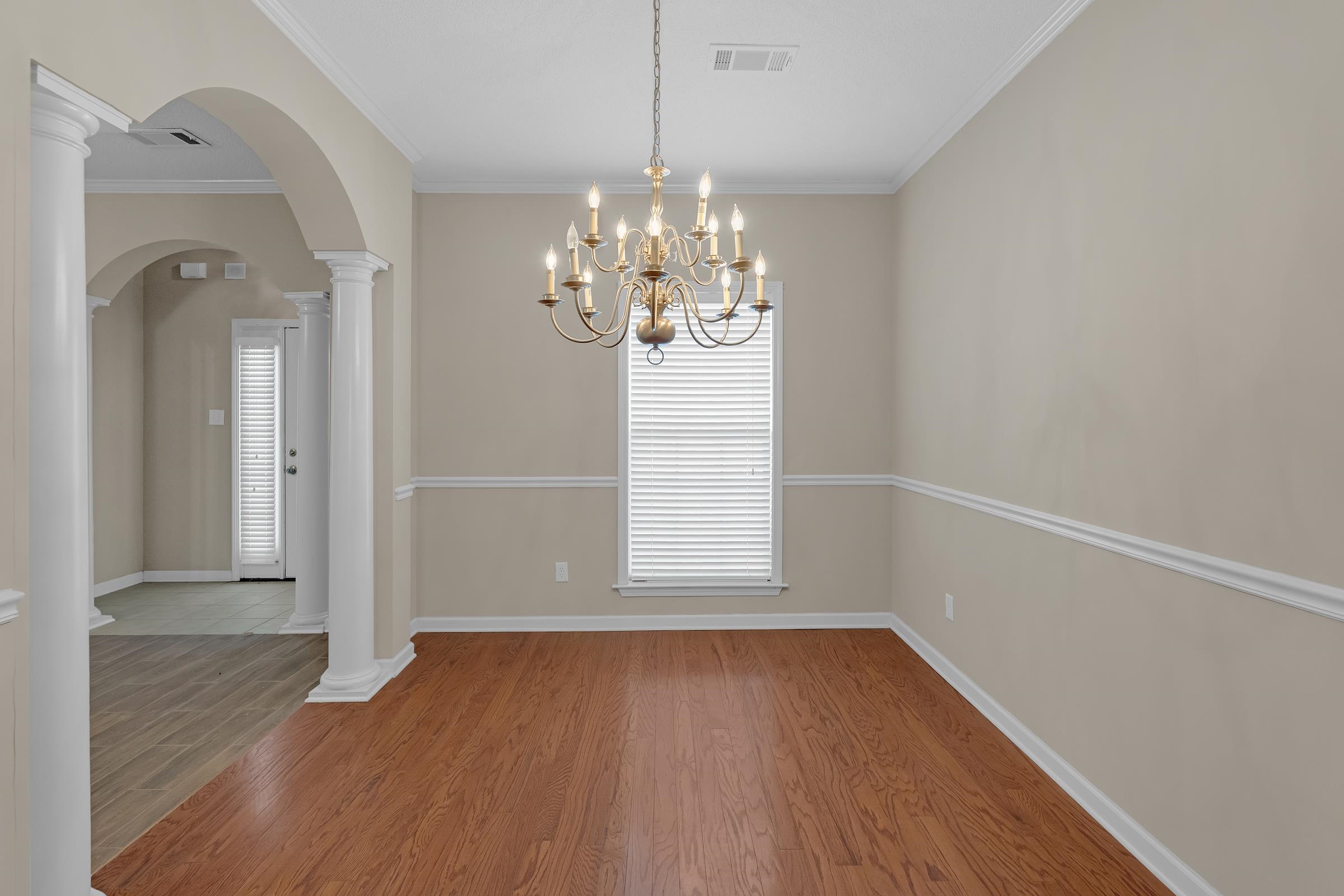 1229 North Sanga Road Memphis, TN 38016 - Photo 4 of 32 Unfurnished dining area featuring crown molding, light wood-style flooring, arched walkways, a chandelier, and decorative columns