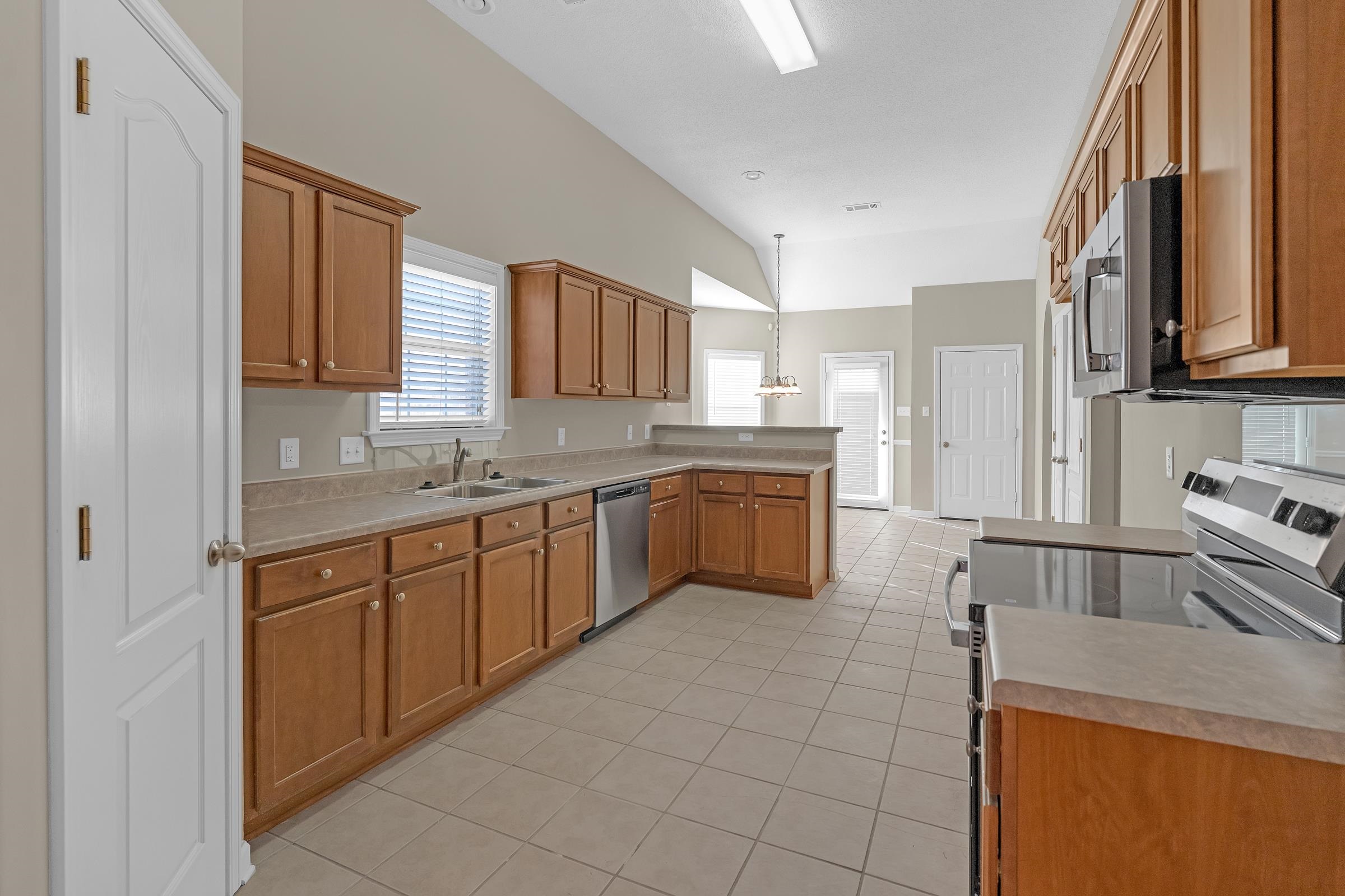 1229 North Sanga Road Memphis, TN 38016 - Photo 6 of 32 Kitchen with appliances with stainless steel finishes, brown cabinets, light tile patterned flooring, hanging light fixtures, and light countertops