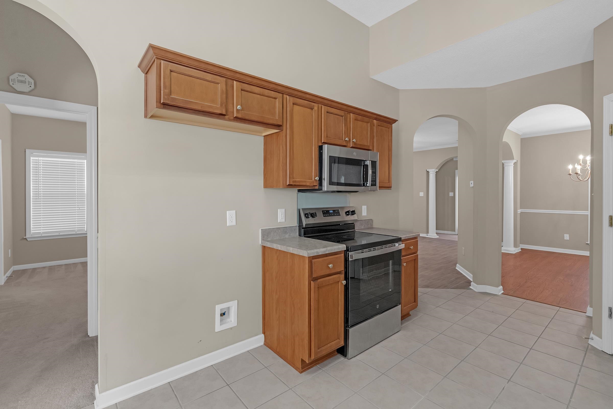 1229 North Sanga Road Memphis, TN 38016 - Photo 7 of 32 Kitchen with arched walkways, appliances with stainless steel finishes, brown cabinetry, light countertops, and light tile patterned flooring