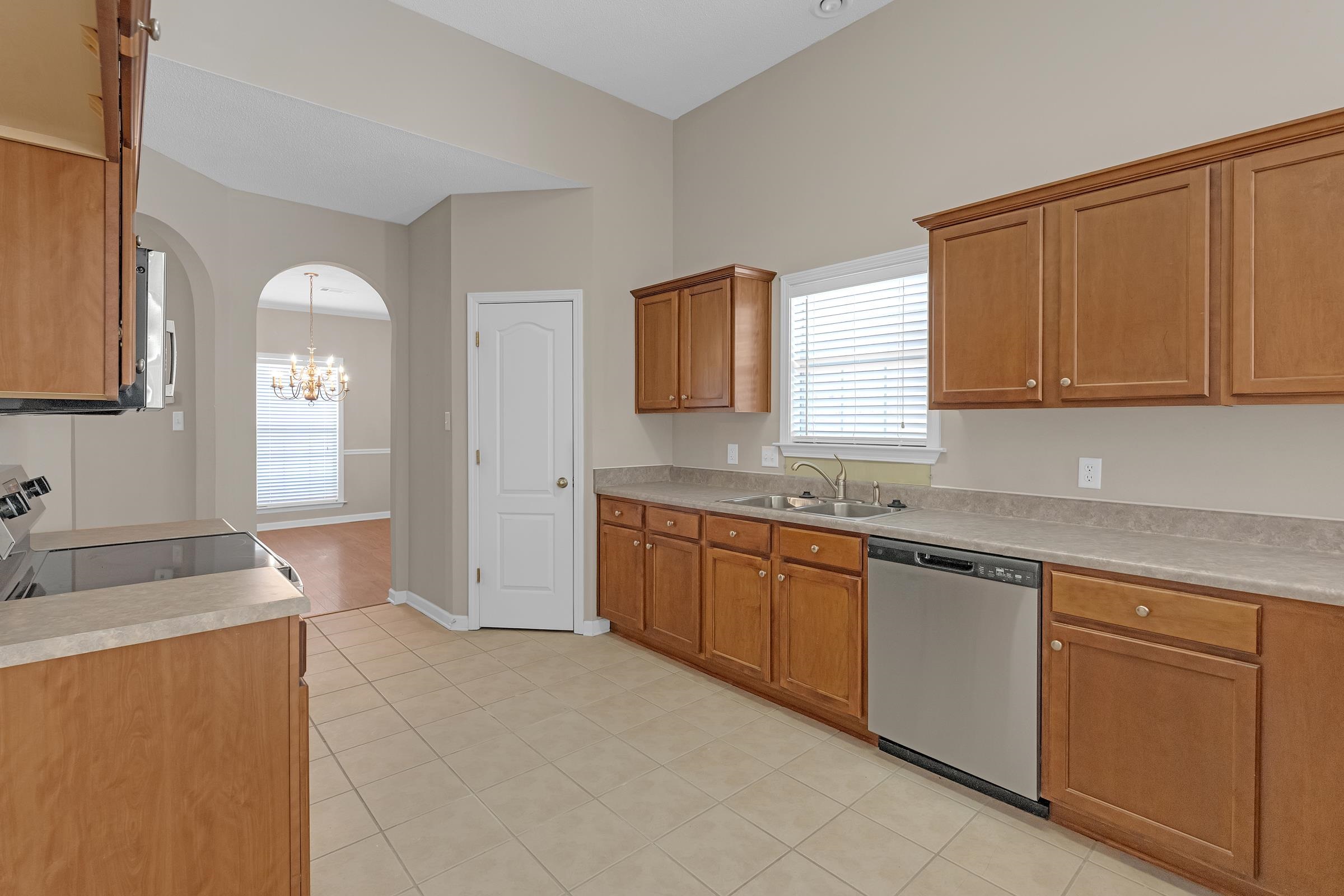 1229 North Sanga Road Memphis, TN 38016 - Photo 8 of 32 Kitchen with arched walkways, brown cabinetry, light countertops, appliances with stainless steel finishes, and light tile patterned flooring