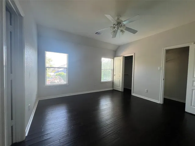 an empty room with wooden floor fan and windows