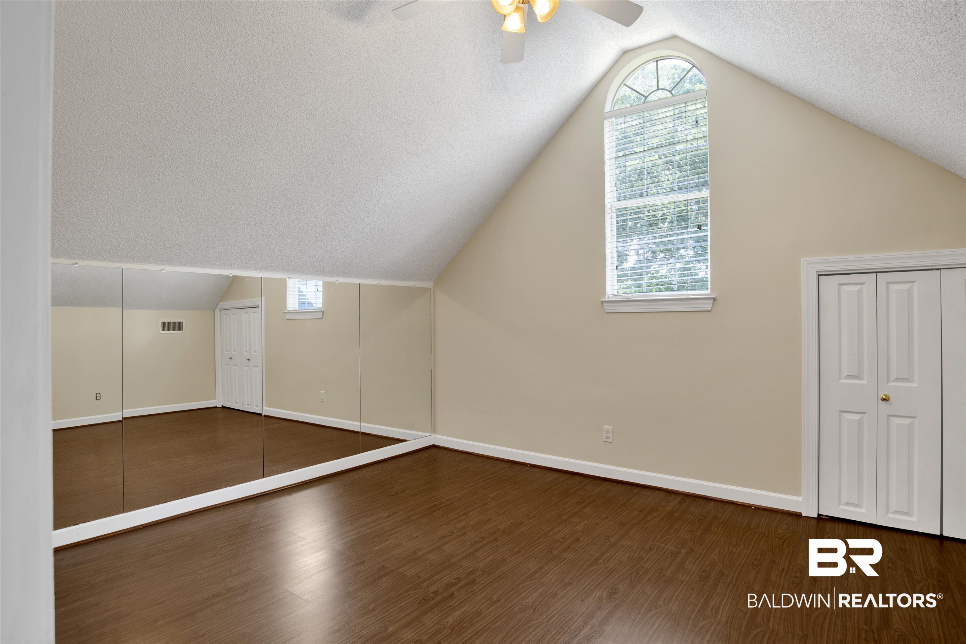 8847 Dawes Lake Road South Mobile, AL 36619 - Photo 30 of 47 Spacious room featuring vaulted ceilings, wood-finish flooring, a prominent arched window, and two sets of bi-fold closet doors
