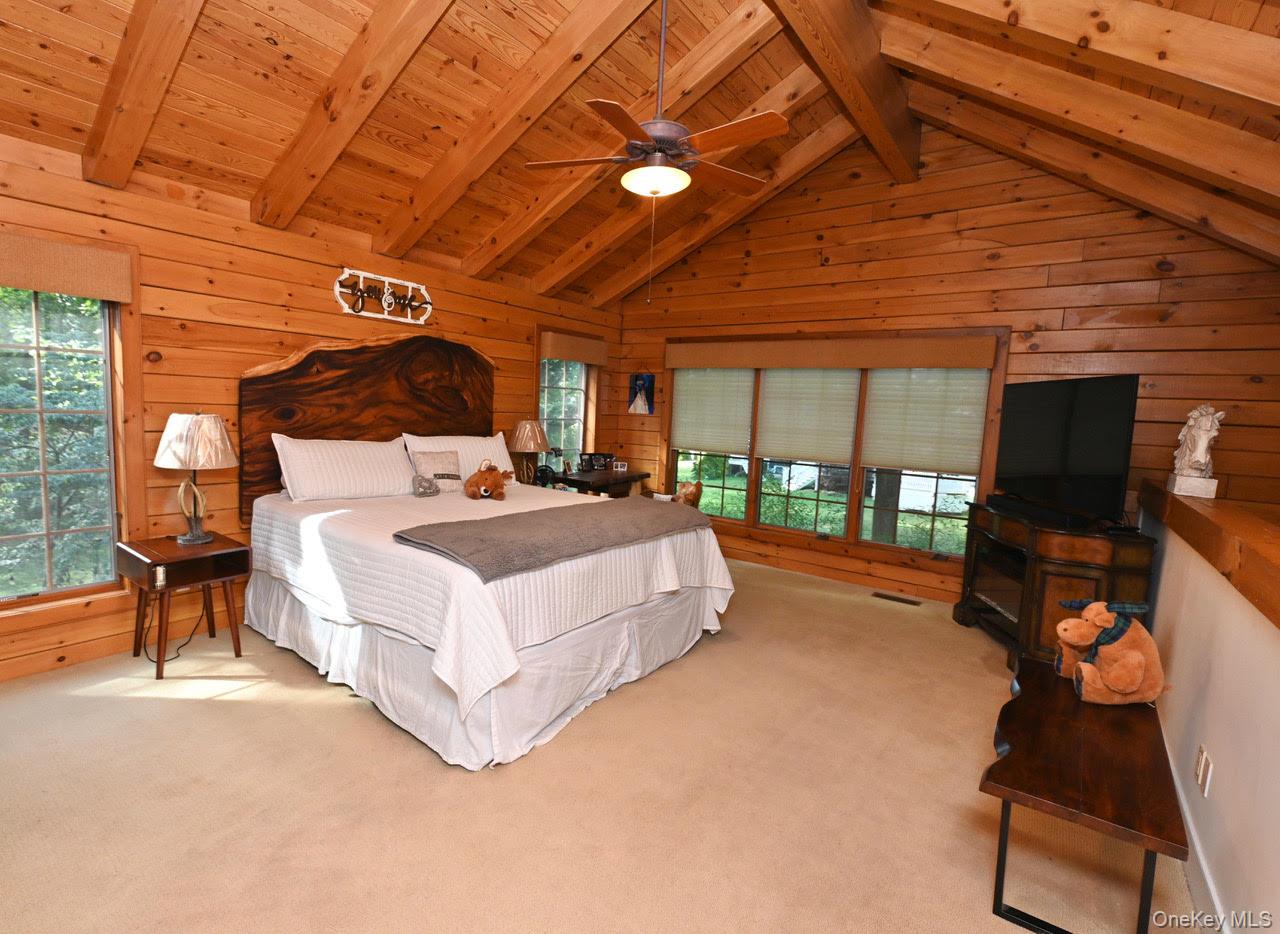216 5th Street St. James, NY 11780 - Photo 13 of 21 Bedroom with wood walls, a wood ceiling with exposed beams, multiple windows, carpet flooring, and ceiling fan
