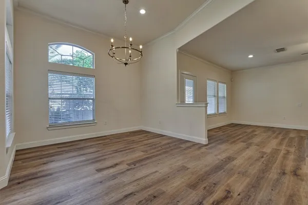 an empty room with wooden floor chandelier and windows