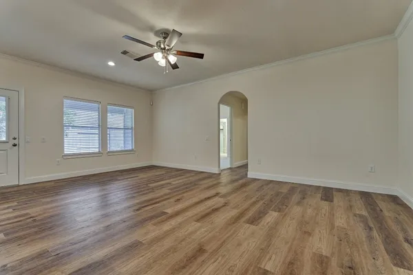 a view of an empty room with wooden floor and fan
