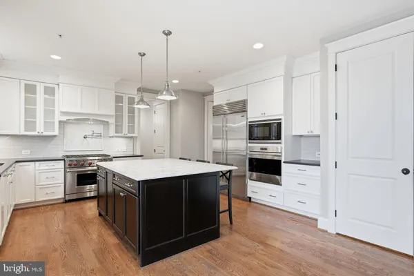 a kitchen with stainless steel appliances kitchen island granite countertop a stove top oven a sink dishwasher and a refrigerator with wooden floor