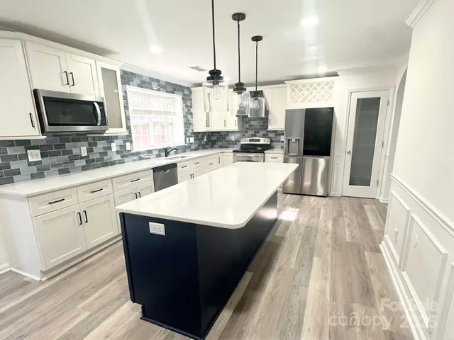 a kitchen with stainless steel appliances a sink dishwasher a stove top oven a refrigerator with wooden floor