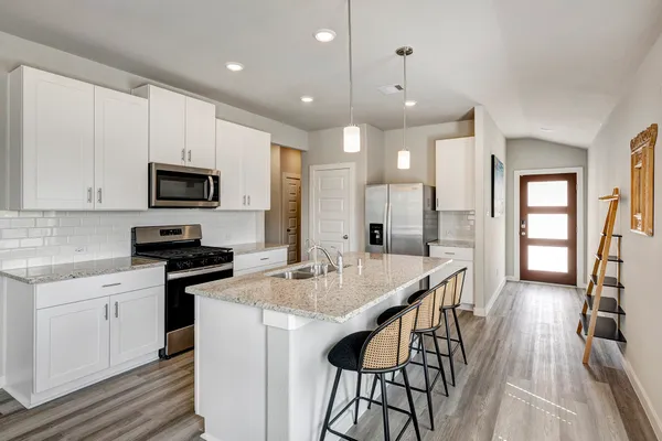 a kitchen with stainless steel appliances granite countertop a stove top oven a sink dishwasher a dining table and chairs with wooden floor