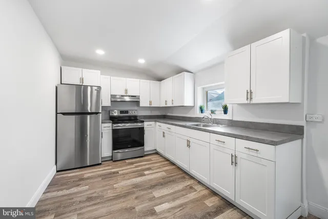 a kitchen with granite countertop a refrigerator oven a sink and white cabinets