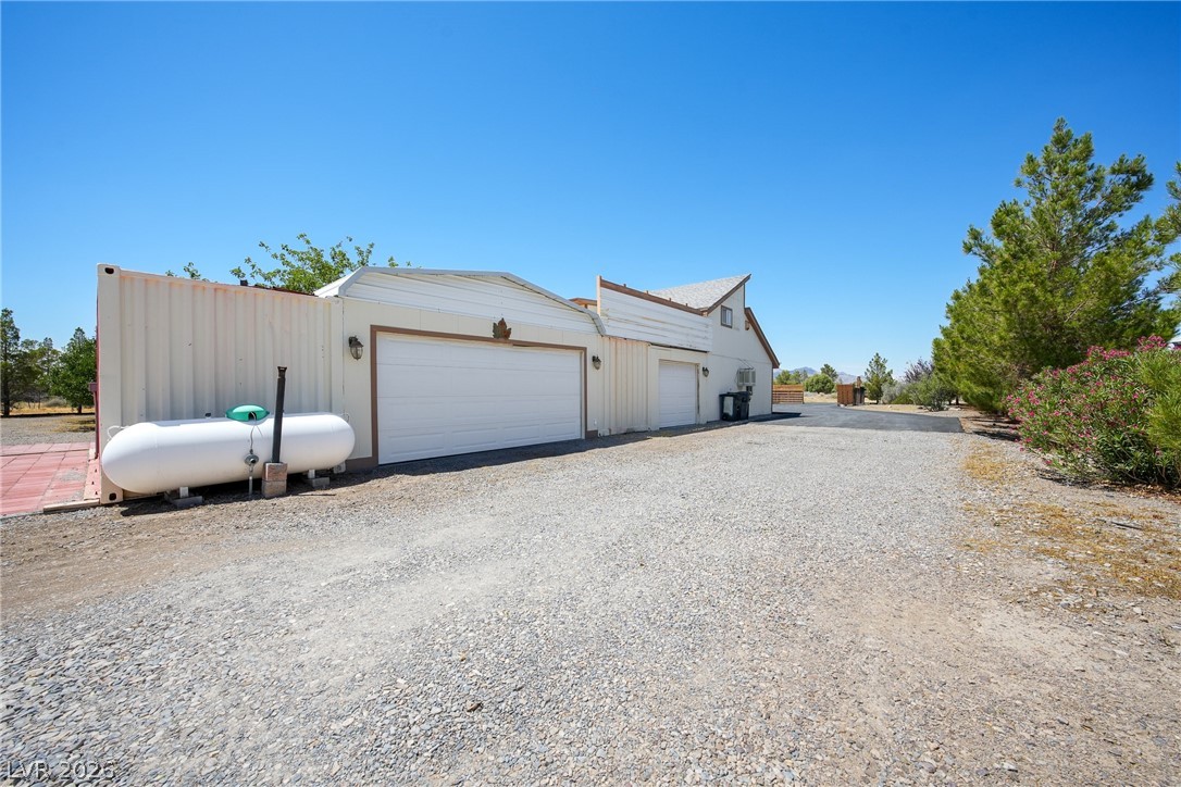 1831 West Horn Road Pahrump, NV 89048 - Photo 41 of 59 A spacious gravel driveway leads to a property featuring multiple garages and mature trees.