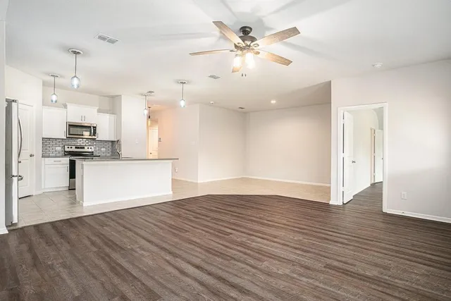 an empty room with wooden floor and kitchen view