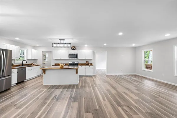 a large kitchen with kitchen island a stove a sink dishwasher a refrigerator and white cabinets with wooden floor