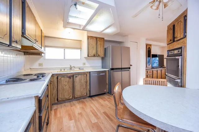 a kitchen with stainless steel appliances granite countertop a refrigerator a sink dishwasher a stove and white countertops with wooden floor