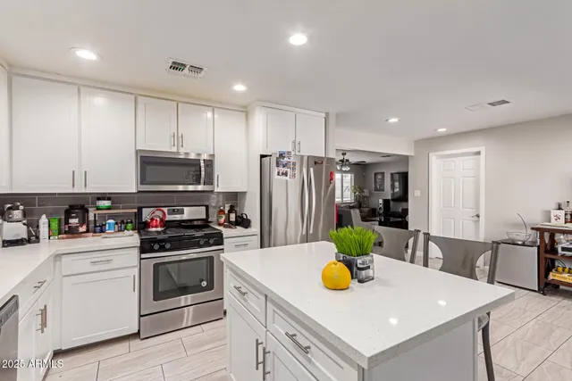 a kitchen with stainless steel appliances kitchen island granite countertop a sink a stove a chimney a refrigerator and white cabinets