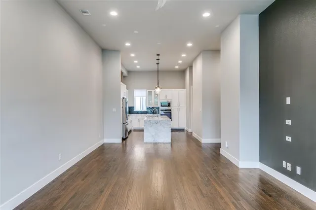 a view of an empty room with wooden floor and a kitchen