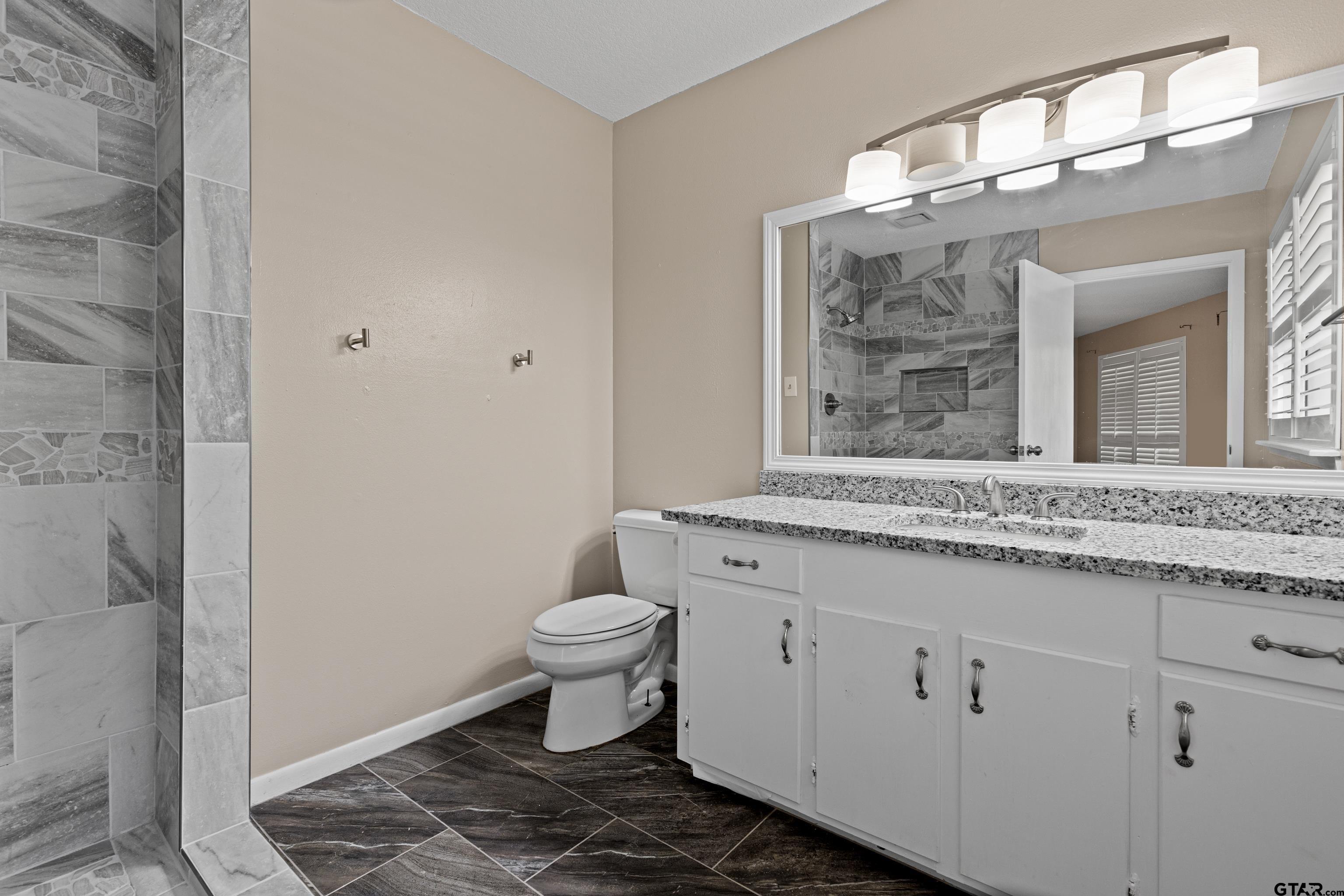 1821 Azalea Street Gilmer, TX 75644 - Photo 16 of 34 a bathroom with a granite countertop toilet a sink and a mirror