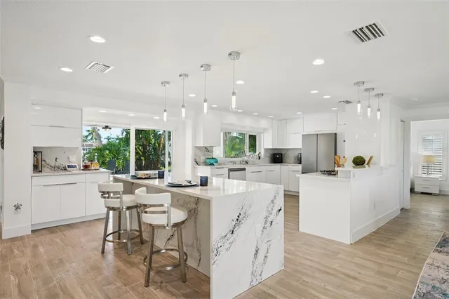 a kitchen with stainless steel appliances kitchen island granite countertop a stove a sink a refrigerator and white cabinets with wooden floor