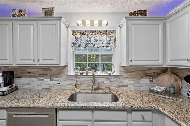 a kitchen with granite countertop a sink a window and cabinets
