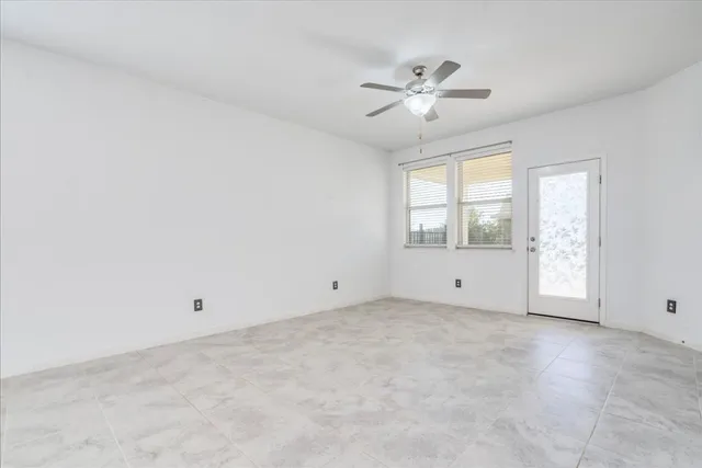 an empty room with chandelier fan and windows