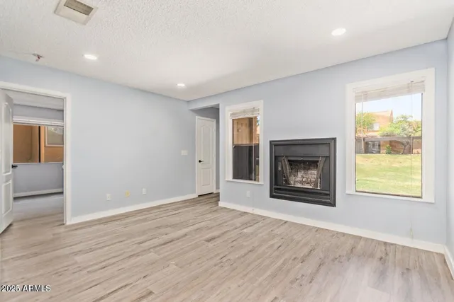 an empty room with wooden floor fireplace and windows