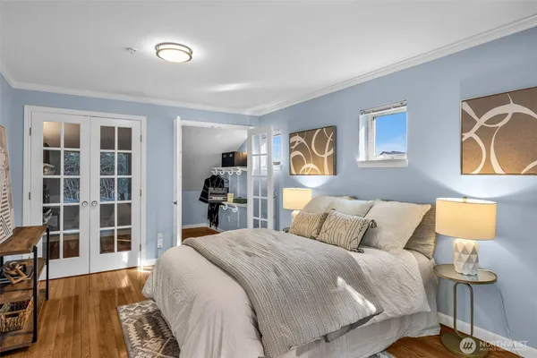 a bedroom with a bed and a lamp on dresser with wooden floor