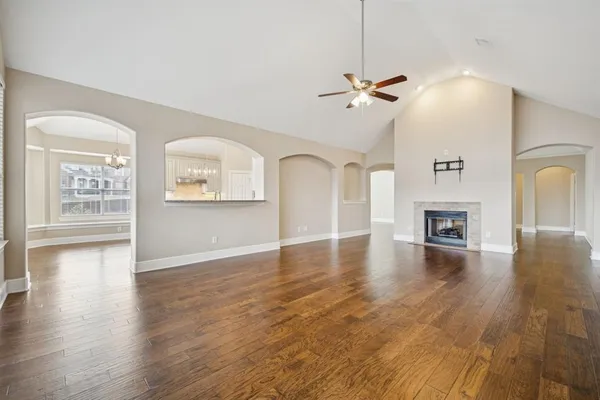 an empty room with wooden floor chandelier fan and windows