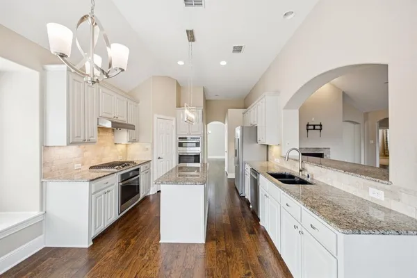 a kitchen with granite countertop a stove a sink a refrigerator and a wooden floor