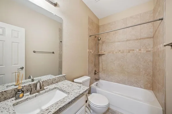 a bathroom with a granite countertop bathtub shower sink vanity mirror and toilet