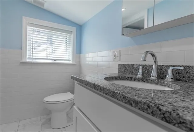 a bathroom with a granite countertop sink a toilet and a window