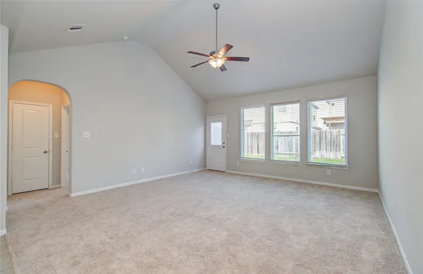 an empty room with a ceiling fan and kitchen view