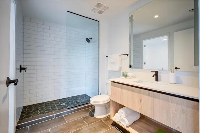 a bathroom with a granite countertop sink a toilet a mirror and shower