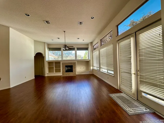 an empty room with wooden floor fireplace and windows