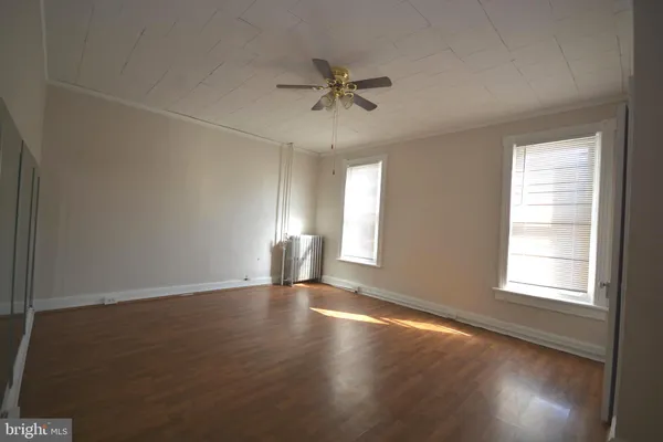 an empty room with wooden floor fan and windows