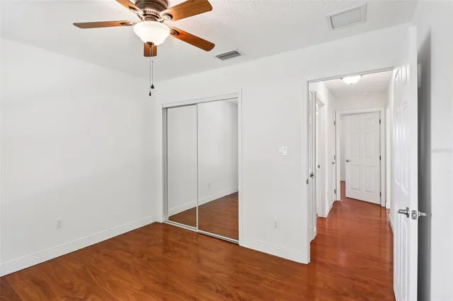 an empty room with wooden floor fan and windows