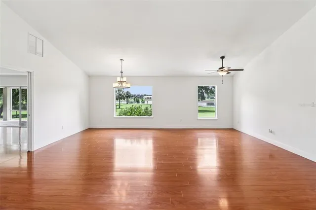 an empty room with wooden floor chandelier and windows