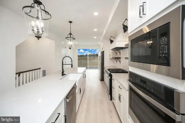 a kitchen with stainless steel appliances kitchen island granite countertop a refrigerator a sink dishwasher and white cabinets with wooden floor