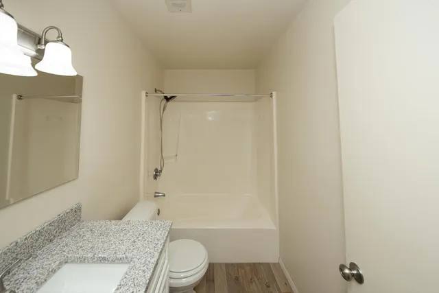 a bathroom with a granite countertop bathtub shower sink vanity and toilet