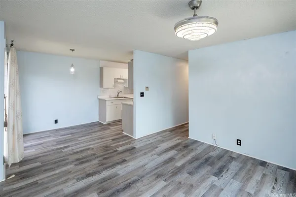 a view of empty room with wooden floor and kitchen view