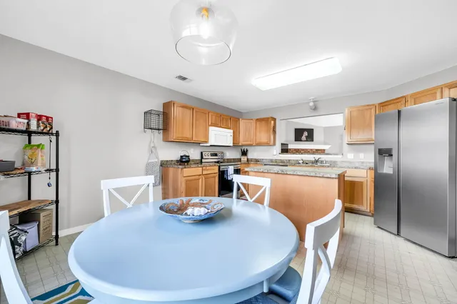 a dining room with stainless steel appliances kitchen island granite countertop a dining table chairs and a refrigerator