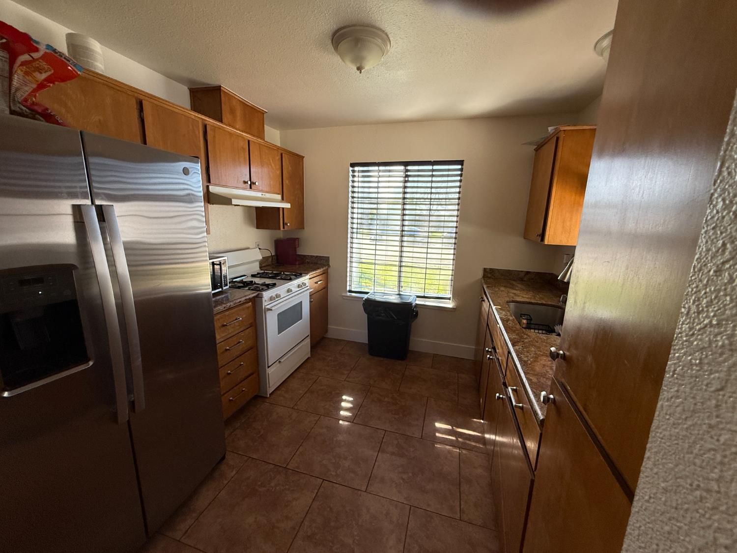 1625 Blue Spruce Way Newman, CA 95360 - Photo 12 of 22 kitchen with stainless steel fridge, a textured ceiling, white range with gas cooktop, brown cabinetry, and dark tile patterned flooring