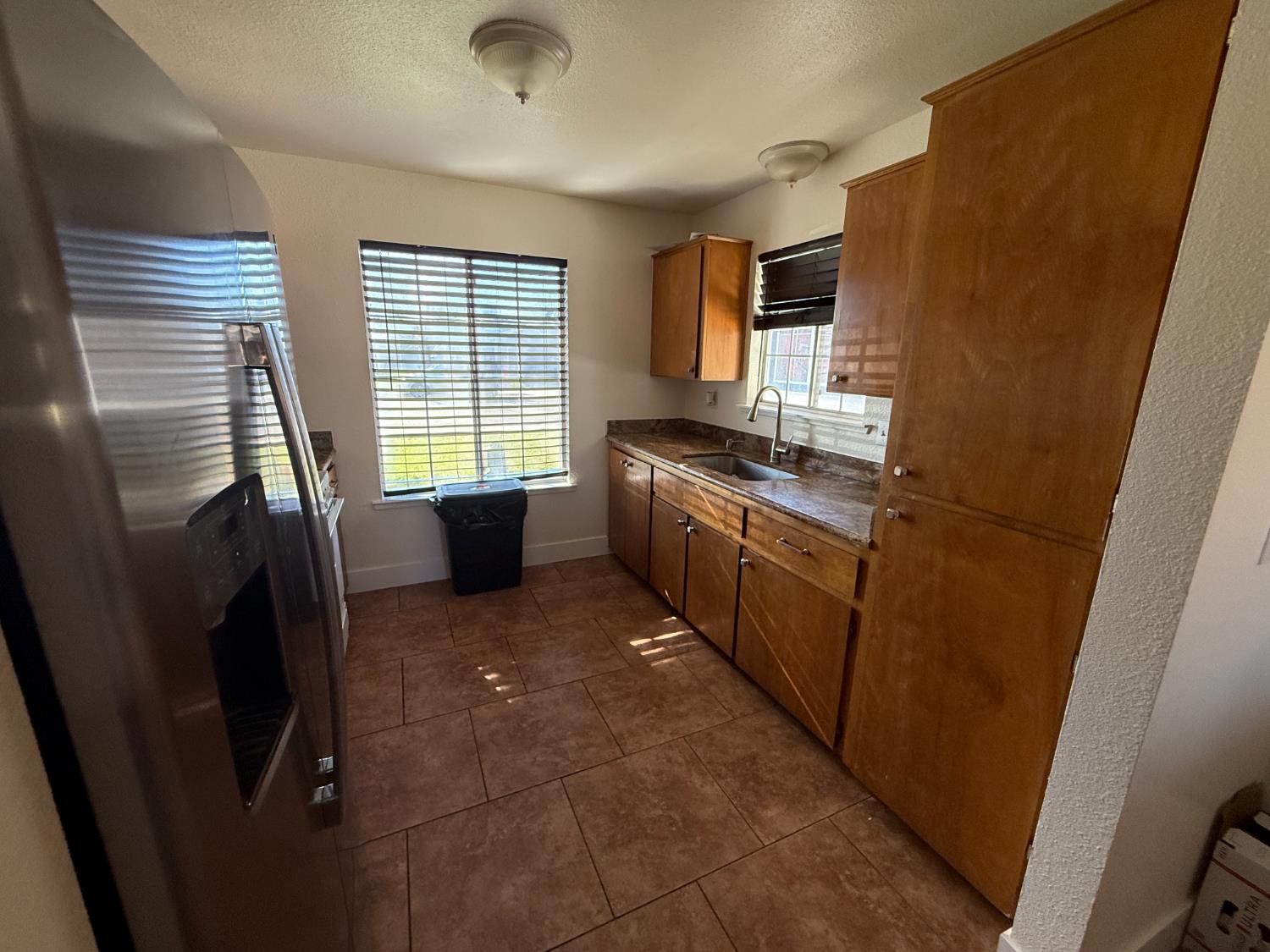 1625 Blue Spruce Way Newman, CA 95360 - Photo 13 of 22 kitchen with stainless steel fridge with ice dispenser, a textured ceiling, dark tile patterned flooring, dark countertops, and brown cabinets