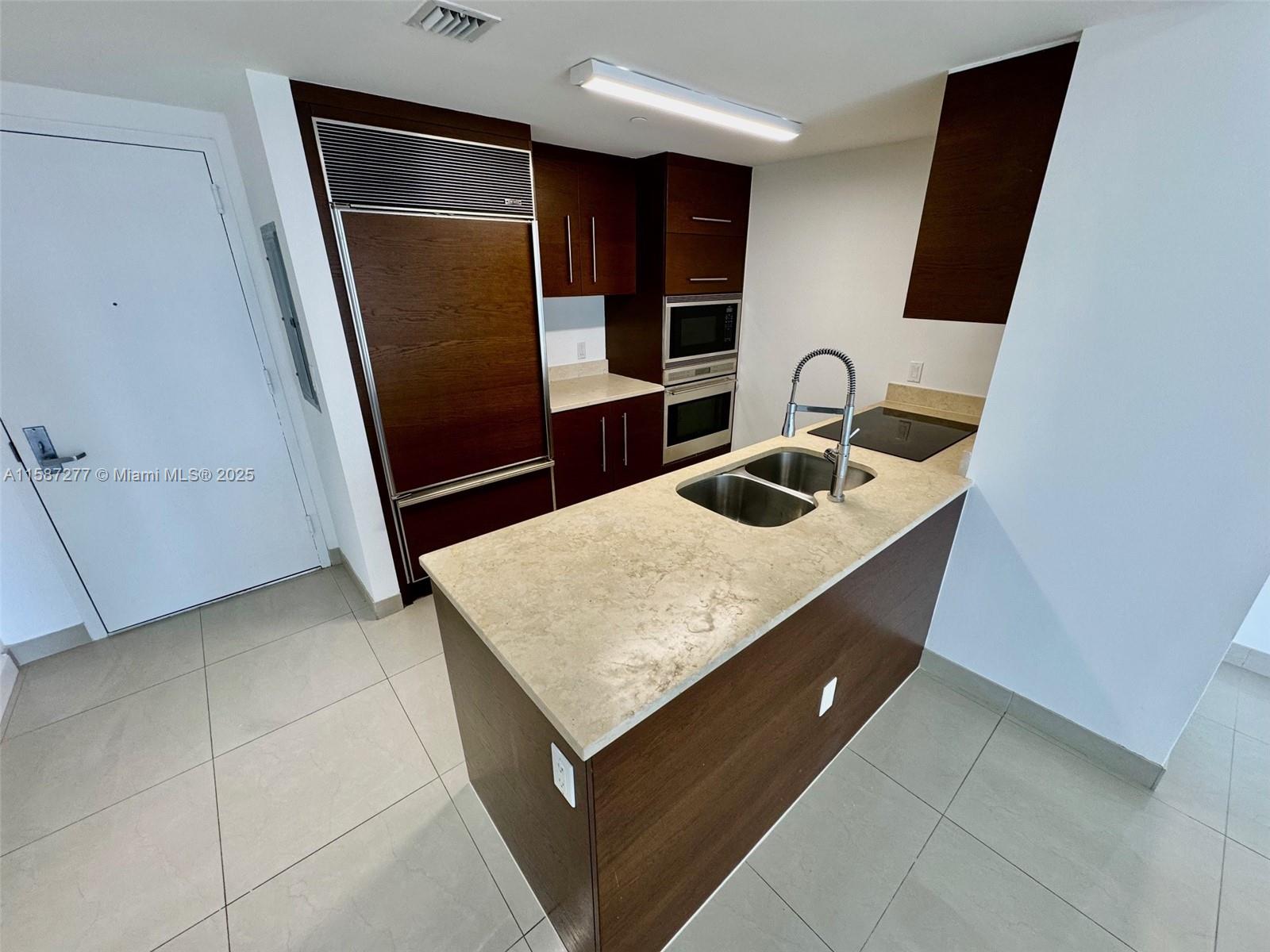 Brickell Miami, FL 33131 - Photo 2 of 15 a kitchen with granite countertop a sink a refrigerator and wooden cabinets