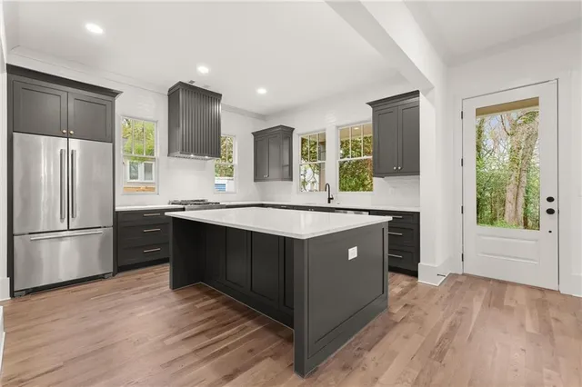 a kitchen with stainless steel appliances granite countertop a refrigerator a sink dishwasher a stove and a large refrigerator with wooden floor