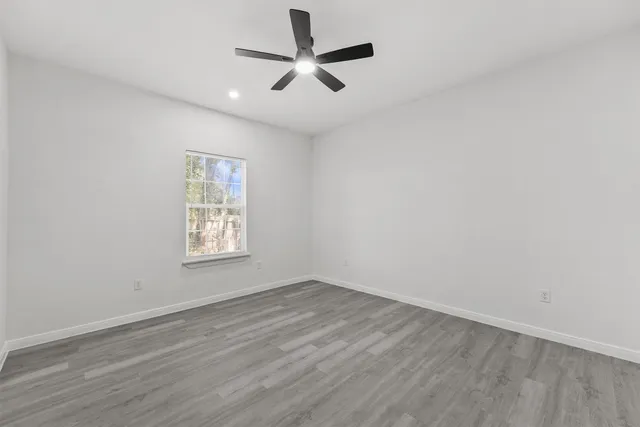 an empty room with wooden floor ceiling fan and windows