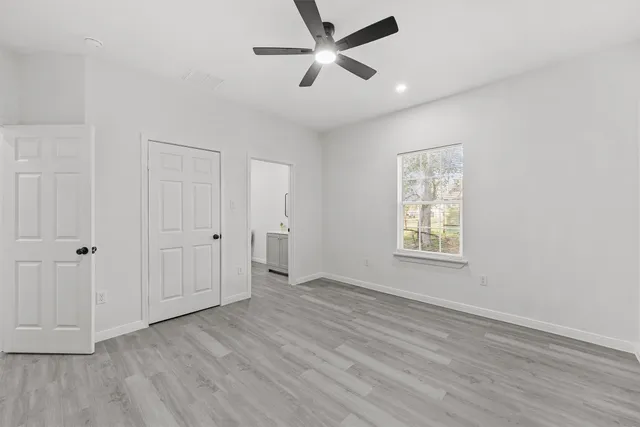an empty room with wooden floor ceiling fan and windows