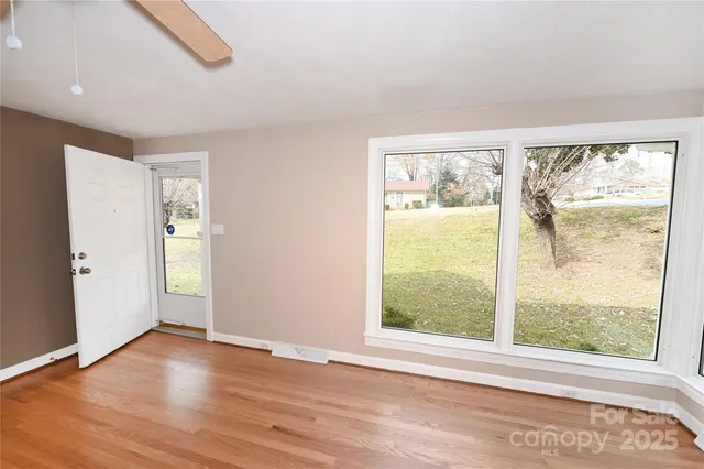 a view of an empty room with wooden floor and a window