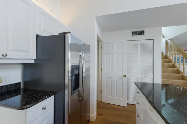 a kitchen with granite countertop a refrigerator a sink and white cabinets