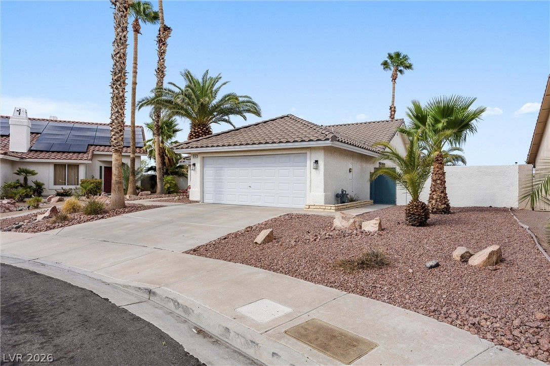 814 Manor Shores Road Henderson, NV 89002 - Photo 38 of 40 Palm trees frame a concrete driveway leading to a classic stucco home with tiled roofing.