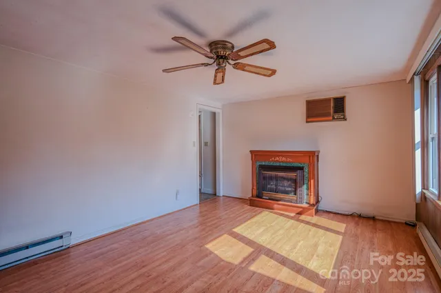 a view of an empty room with wooden floor fireplace and a window